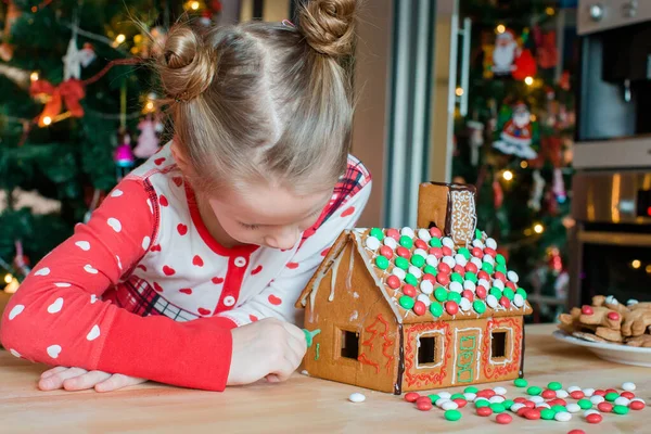 Little girls podejmowania Christmas domek piernika przy kominku w urządzonym salonie. — Zdjęcie stockowe