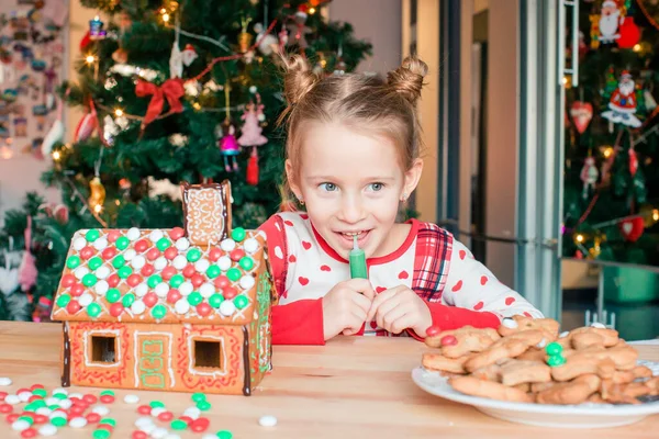 Kleine Mädchen basteln Weihnachts-Lebkuchenhaus am Kamin im geschmückten Wohnzimmer. — Stockfoto