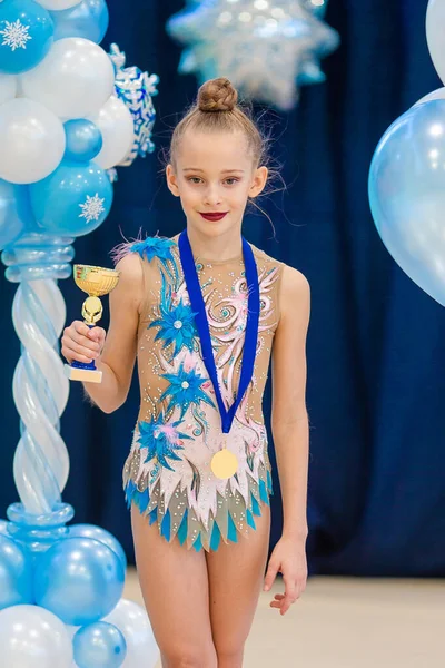 Petite gymnaste avec ses récompenses sportives sur le tapis en gymnastique rythmique — Photo