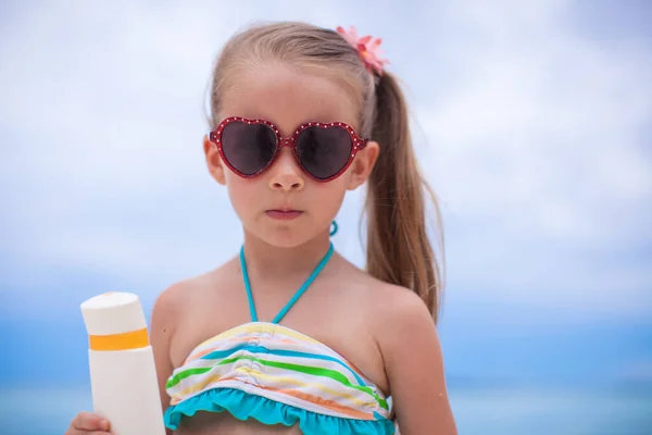 Portrait of Little adorable girl in swimsuit holds suntan lotion bottle — Stock Photo, Image