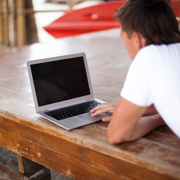 Achteraanzicht van jonge man met laptop buiten op vakantie — Stockfoto