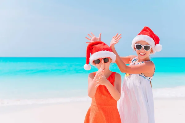 Piccole ragazze adorabili a Babbo Natale cappelli durante le vacanze di Natale in spiaggia divertirsi insieme — Foto Stock