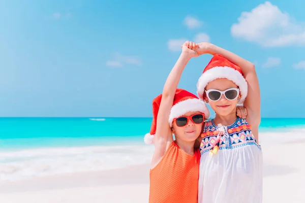 Kleine entzückende Mädchen in Weihnachtsmützen während des Weihnachtsurlaubs am Strand, die zusammen Spaß haben — Stockfoto