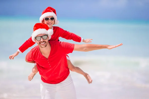 พ่อกับลูกสาวในซานต้าแฮทสนุกกันที่ชายหาดเขตร้อน — ภาพถ่ายสต็อก