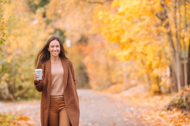 Sonbahar konsepti: Sonbahar parkında sonbahar yaprakları altında kahve içen güzel bir kadın.