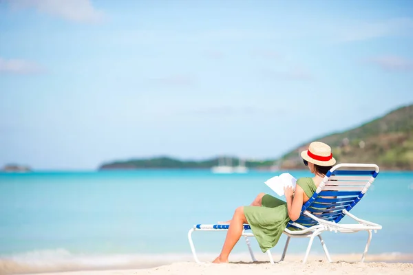 Joven mujer leyendo libro sobre chaise-lounge en la playa — Foto de Stock