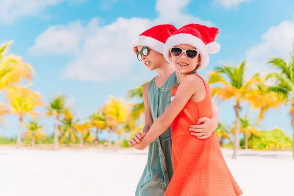 Little adorable girls in Santa hats during beach Christmas vacation having fun together — Stock Photo, Image