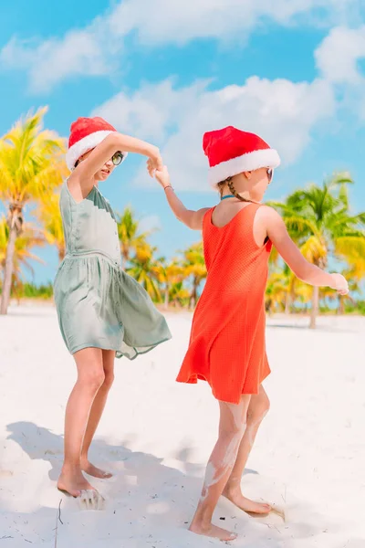 Piccole ragazze adorabili a Babbo Natale cappelli durante le vacanze di Natale in spiaggia divertirsi insieme — Foto Stock