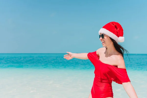Noel Baba şapkası yürüyen genç kadın ellerinin beyaz kumlu plaj üzerinde yayılmış — Stok fotoğraf