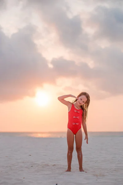 Entzückend glückliches kleines Mädchen am weißen Strand bei Sonnenuntergang. — Stockfoto