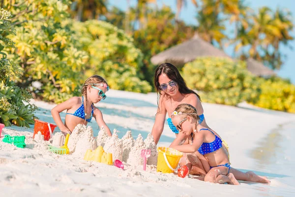 Matka i małe córeczki robiące zamek z piasku na tropikalnej plaży — Zdjęcie stockowe