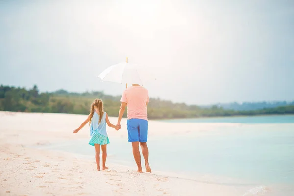 Unge far och hans lilla dotter går under paraply på vit sandstrand — Stockfoto