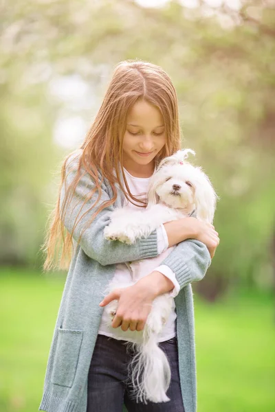 Pequena menina sorridente brincando e abraçando filhote de cachorro no parque — Fotografia de Stock