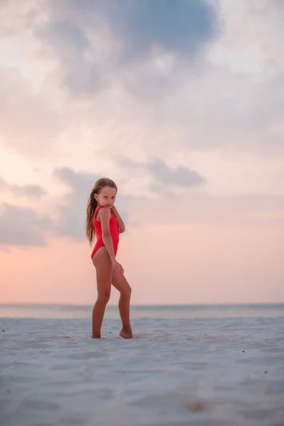Entzückend glückliches kleines Mädchen am weißen Strand bei Sonnenuntergang. — Stockfoto