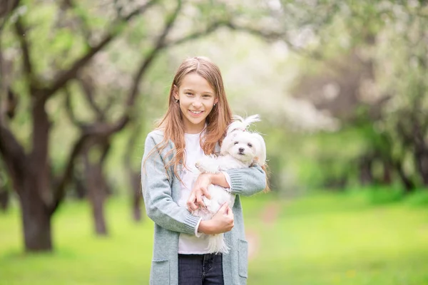 Pequena menina sorridente brincando e abraçando filhote de cachorro no parque — Fotografia de Stock