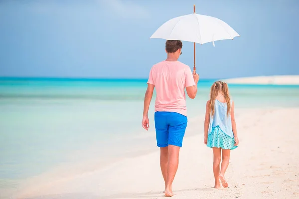 Young father and his little daughter walking under umbrella on white sand beach — Stock Photo, Image