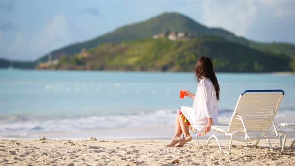 Jonge vrouw met cocktail glas op wit strand zitten op zonnebank — Stockvideo