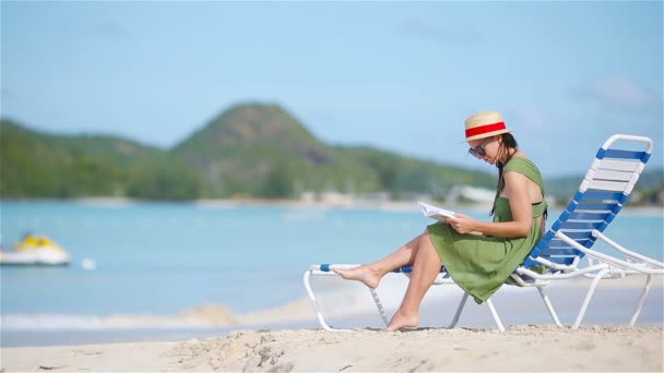 Mujer joven leyendo libro sobre tumbonas durante la playa tropical blanca — Vídeo de stock