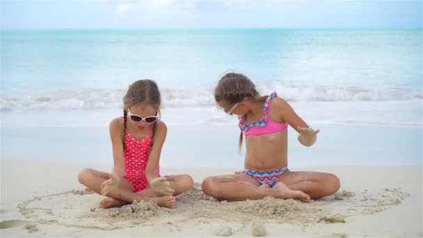 Imádnivaló kislányok játszanak homokkal a parton. Gyerekek ülnek a sekély vízben és homokvárat építenek. — Stock videók