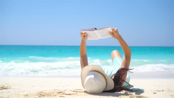 Молода жінка читає на тропічному білому пляжі — стокове відео