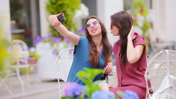 İki genç kız açık hava kafede akıllı telefondan selfie çekiyor.. — Stok video