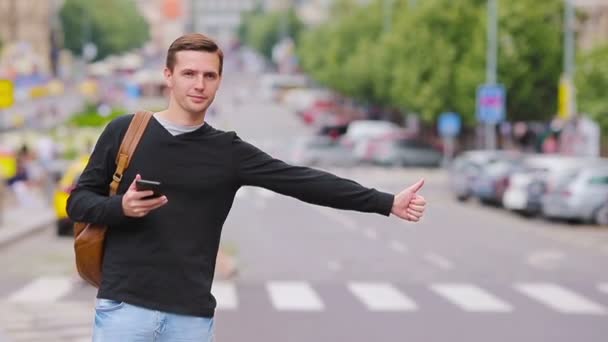 Junger glücklicher Mann nimmt in europäischen Straßen ein Taxi. Porträt eines kaukasischen Touristen mit einem lächelnden Rucksack und einem Taxi — Stockvideo