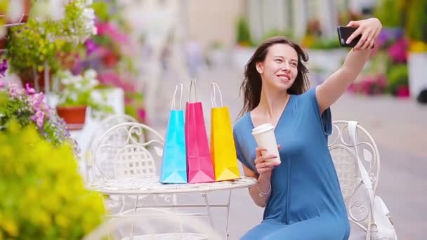 Moda chica feliz con bolsas después de comprar tomando selfie en la cafetería al aire libre. Venta, consumismo y concepto de personas. Caucásico chica disfrutar caliente día en al aire libre café . — Vídeo de stock