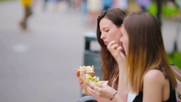 Las mujeres caucásicas comen hamburguesas sándwich de comida rápida en la calle al aire libre. Chicas activas hambrientas y comiendo comida callejera después de un largo paseo — Vídeos de Stock