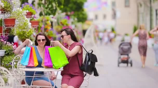 Dos compradores de moda mujer con bolsas de compras en la calle. Venta, consumismo y concepto de personas. chicas caucásicas disfrutan de su día cálido en la cafetería al aire libre . — Vídeo de stock