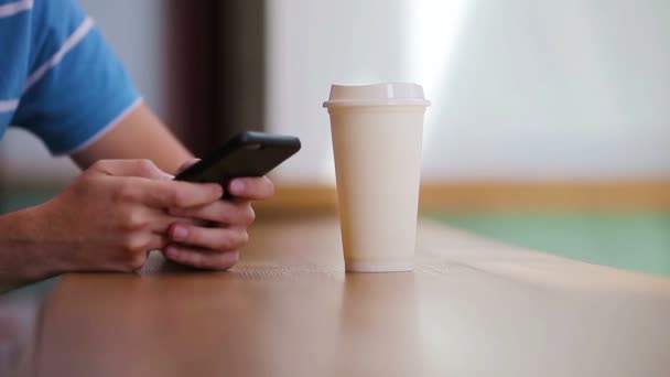 Gros plan de mains masculines tenant un téléphone portable et un verre de café dans un café. Homme utilisant un smartphone mobile. Garçon touchant un écran de son intelligence. Fond flou, horizontal . — Video