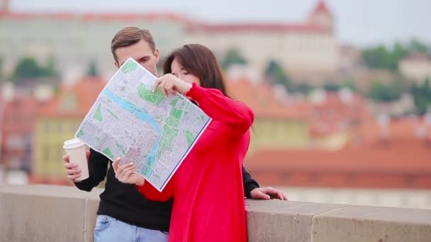 Νεαρό ζευγάρι τουριστών που ταξιδεύουν σε διακοπές στην Ευρώπη χαμογελώντας ευτυχισμένοι. Καυκάσια οικογένεια με χάρτη της πόλης σε αναζήτηση αξιοθέατα — Αρχείο Βίντεο