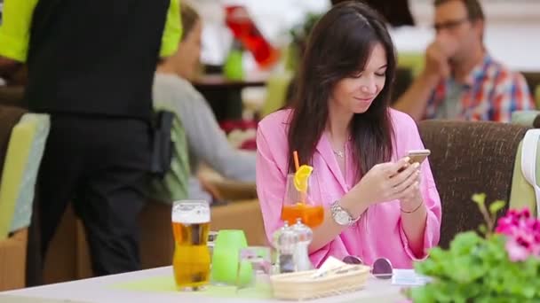 Молода красива жінка сидить у кафе, п'є смачний коктейль і відправляє повідомлення. Щасливий турист насолоджується європейськими канікулами на олімпійських іграх — стокове відео