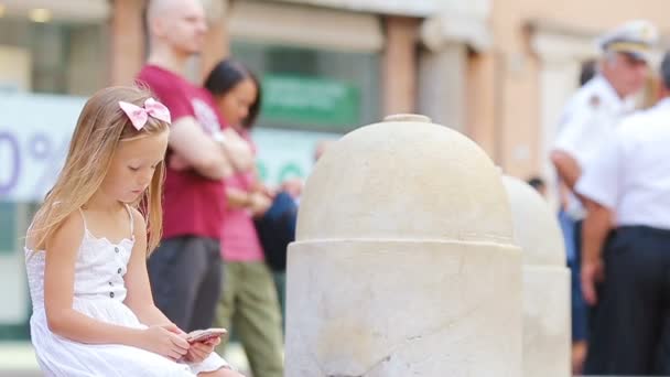 Приваблива маленька дівчинка з смартфоном на вулиці в місті Европії поблизу відомої Фонтани ді Треві. — стокове відео