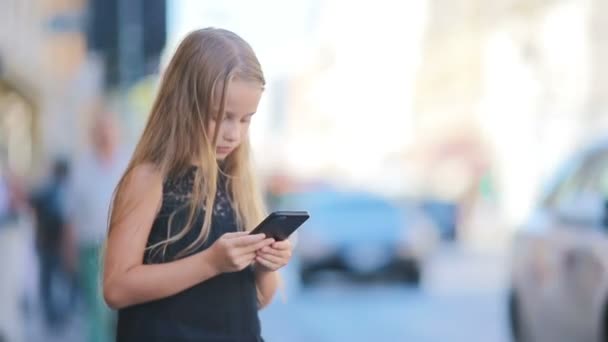 Schattig klein meisje met smartphone op warme dag buiten in europese stad — Stockvideo