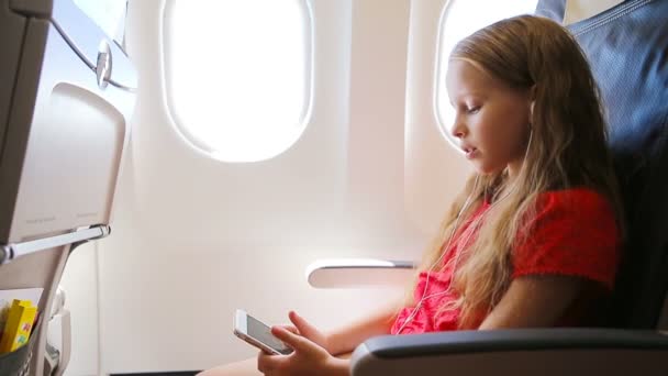 Menina adorável viajando de avião sentado perto da janela. Kid ouvindo música sentada perto da janela da aeronave — Vídeo de Stock