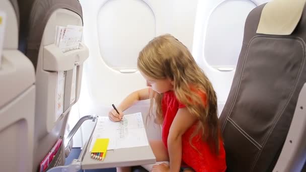Entzückendes kleines Mädchen, das mit dem Flugzeug unterwegs ist. Kind zeichnet Bild mit bunten Bleistiften, die in der Nähe des Flugzeugfensters sitzen — Stockvideo