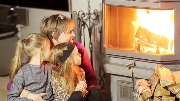 Mormor och hennes två små barnbarn sitter vid en öppen spis i sitt familjehem på julafton — Stockvideo