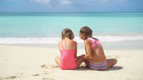 Underbara små flickor som leker med sand på stranden. Bakåt syn på barn som sitter i grunt vatten och göra ett sandslott. — Stockvideo