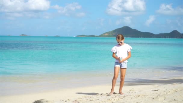 Petite fille avec bouteille de crème solaire assise à la plage tropicale — Video
