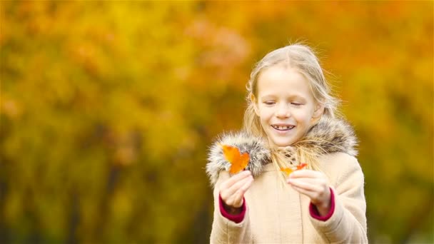 Portrait of adorable little girl outdoors at beautiful warm day with yellow leaf in fall — Stock Video