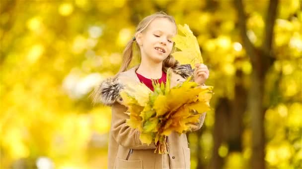 Portrait of adorable little girl outdoors at beautiful warm day with yellow leaf in fall — Stock Video