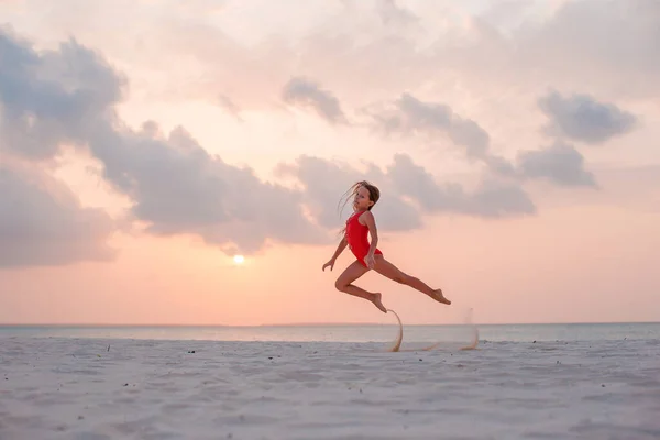 Entzückend glückliches kleines Mädchen am weißen Strand bei Sonnenuntergang. — Stockfoto