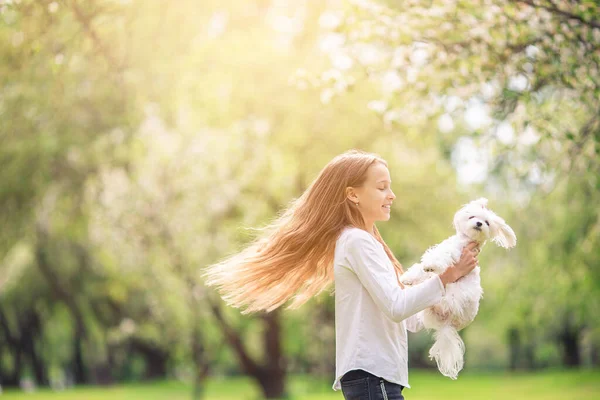 Küçük gülümseyen kız parkta oynaşıyor ve yavru köpeğe sarılıyor. — Stok fotoğraf