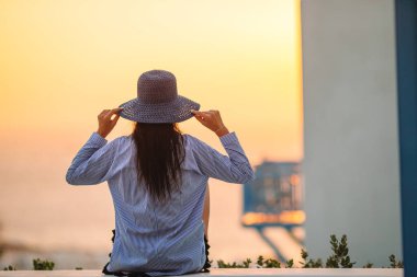 Genç bir kadın ünlü bir köy olan Mykonos 'ta gün batımına bakıyor.