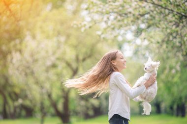 Küçük gülümseyen kız parkta oynaşıyor ve yavru köpeğe sarılıyor.