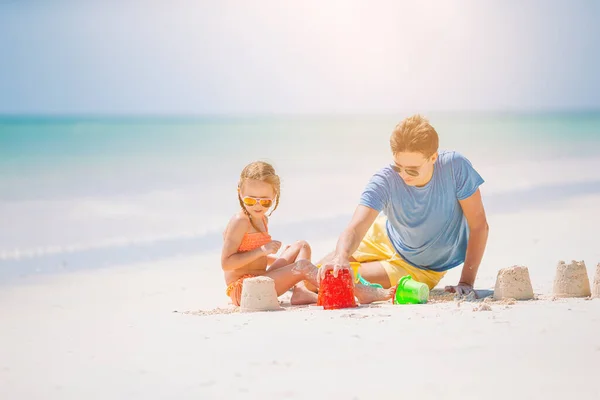 Ojciec i dzieci robią zamek z piasku na tropikalnej plaży. Zabawa rodzinna zabawkami plażowymi — Zdjęcie stockowe