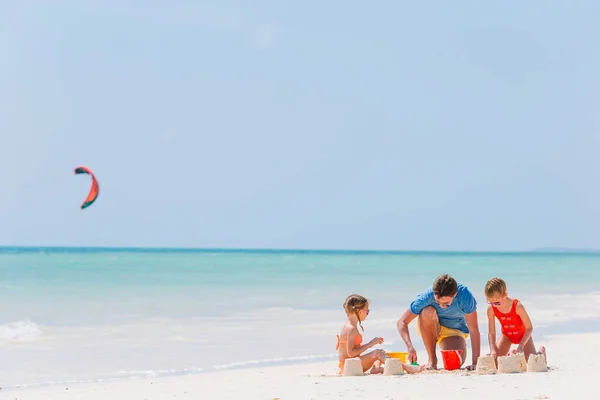 Padre e hijos haciendo castillo de arena en la playa tropical. Familia jugando con juguetes de playa —  Fotos de Stock