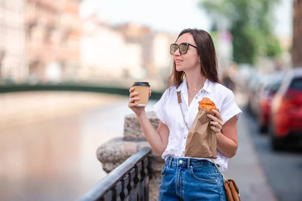遊歩道の屋外でクロワッサンとコーヒーを持つ女性 — ストック写真