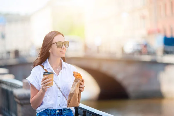 遊歩道の屋外でクロワッサンとコーヒーを持つ女性 — ストック写真