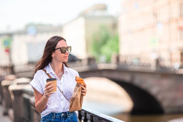 遊歩道の屋外でクロワッサンとコーヒーを持つ女性 — ストック写真